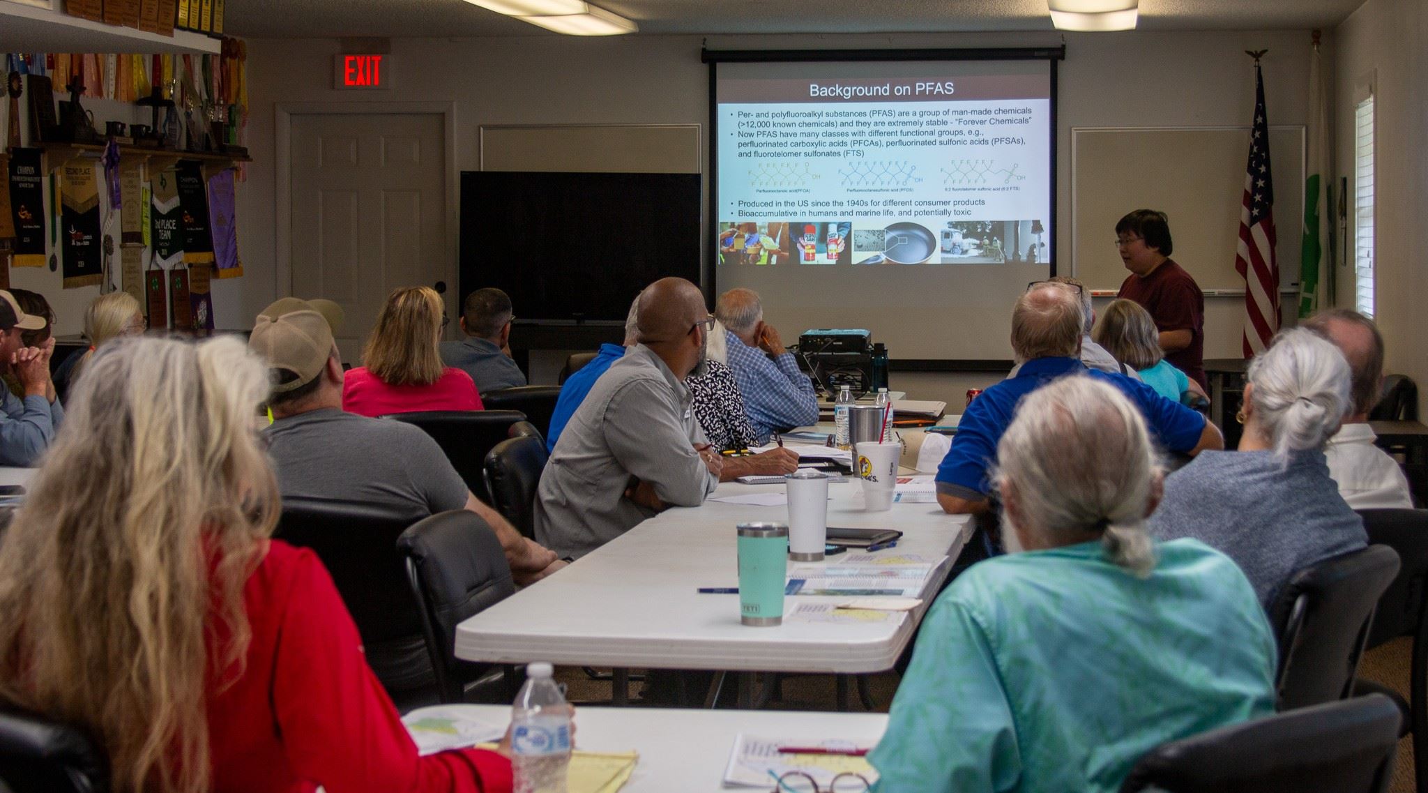 Image of people sitting at long tables watching a presentation ona screen